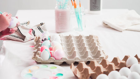 Little girl painting craft Easter eggs with acrilic paint.