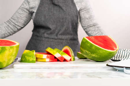 Slicing red seedless watermelon on a white cutting board.の写真素材