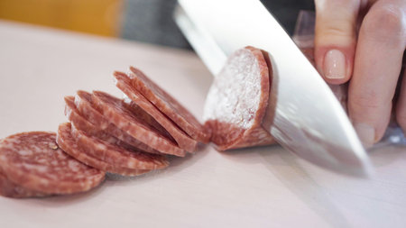 Slicing salami into thin rings ona  white cutting board.