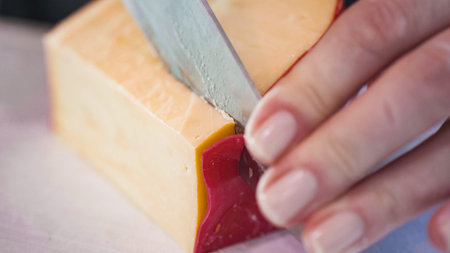 Slicing gouda cheese into small cubes on a white cutting board.