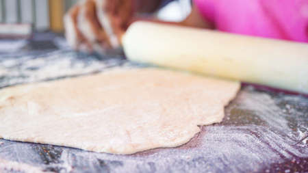 Little girl rolling out pizza dough with help of the aunt for individual small pizzas.の写真素材