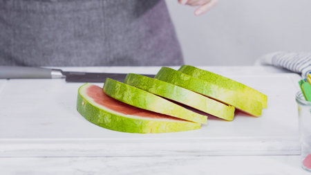 Slicing red watermelon into small pieces on a white cutting board.