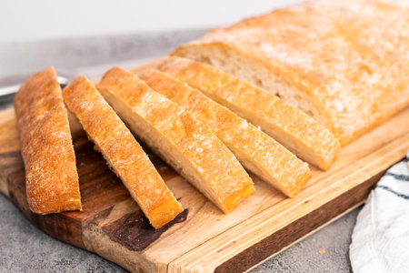 Sliced loaf of freshly baked ciabatta bread on gray table.