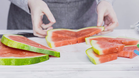 Slicing red watermelon into small pieces on a white cutting board.