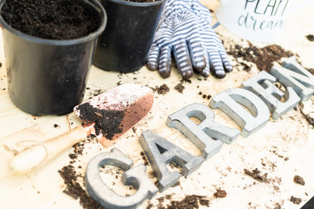 Sign GARDEN in metal letters around spilled soil and planting pots on a wooden garden table.の写真素材