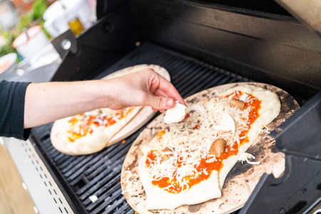 Preparing individual grilled pizzas on an outdoor gas grill.の写真素材