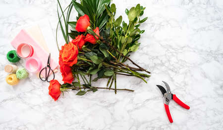 Flat lay. Florist pruning red roses with small shears for arranging bouquets.の写真素材