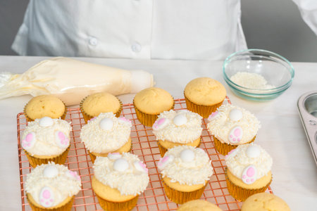 Decorating vanilla cupcakes with a white buttercream icing and bunny ears for Easter.