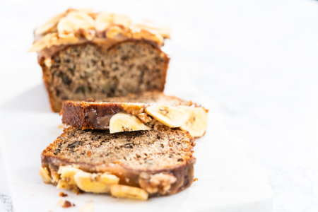 Sliced banana nut bread with drizzled with homemade caramel on a marble cutting board.