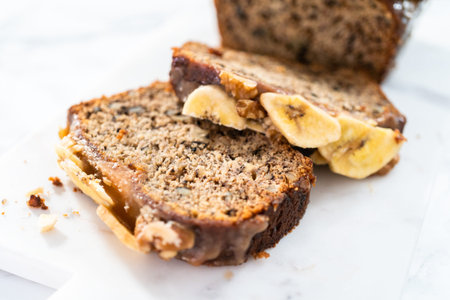 Sliced banana nut bread with drizzled with homemade caramel on a marble cutting board.