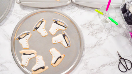 Flat lay. Decorating ice skate shaped sugar cookies with black color royal icing.