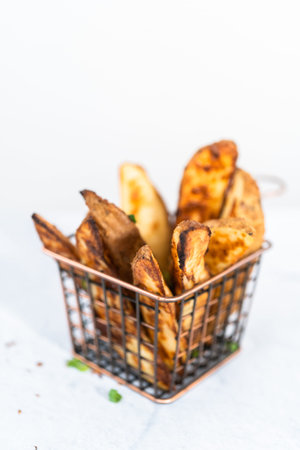 Freshly baked potato wedges with spices in a wire basket.