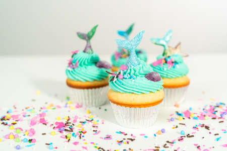 Gourmet mermaid cupcakes topped with blue buttercream frosting and decorated with sprinkles and chocolate mermaid tails.の写真素材