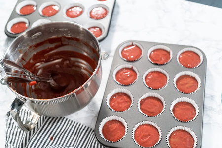 Scooping cupcake batter into a cupcake pan to bake red velvet cupcakes.