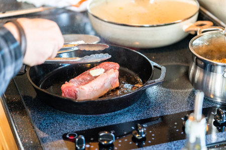 Frying New York strip steak in cast iron frying pan over the electric stove.