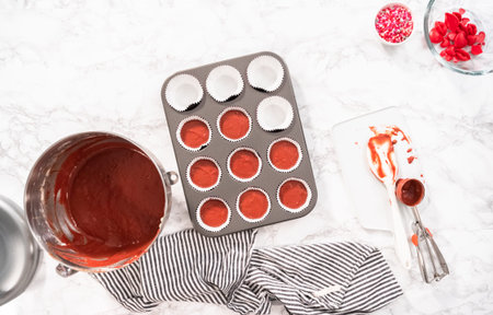 Flat lay. Flat lay. Scooping cupcake batter into a cupcake pan to bake red velvet cupcakes.