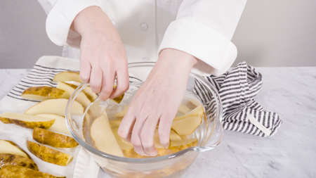 Step by step. Soaking potato wedges in a bowl of water to prepare baked potato wedges with spices.の写真素材