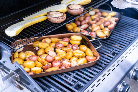 Grilling small potatoes with slices of garlic on an outdoor gas grill.