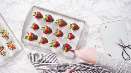 Drizzling melted chocolate from pastry piping bag to chocolate covered strawberries.の写真素材