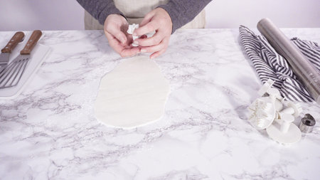 Step by step. Cutting out snowflakes with cookie cutters out of white fondant on a marble counter.