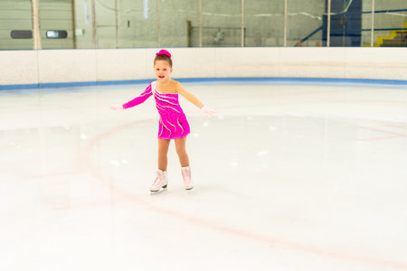 Little figure skater in pink dress practicing on the indoor ice rink.の写真素材