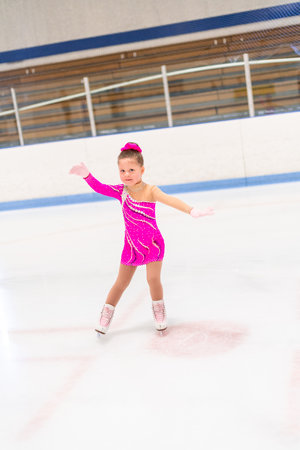 Little figure skater in pink dress practicing on the indoor ice rink.の写真素材