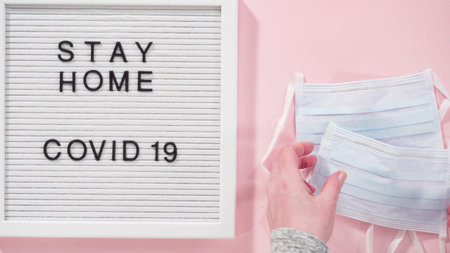 Flat lay. STAY HOME and COVID-19 sign on message board with a blue medical mask.の写真素材