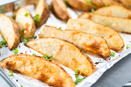 Freshly baked potato wedges with spices on a baking sheet.