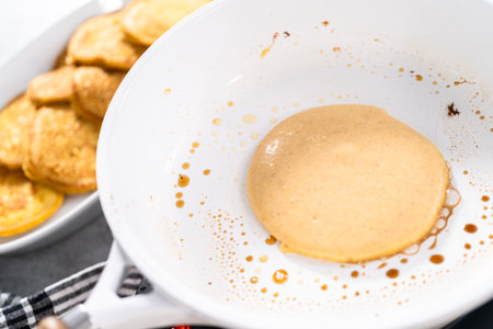 Frying pumpkin pancakes batter on a white frying pan.の写真素材