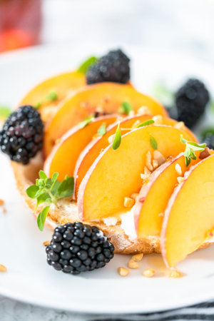 Peach ricotta toast garnished with blackberries on a white plate.の写真素材