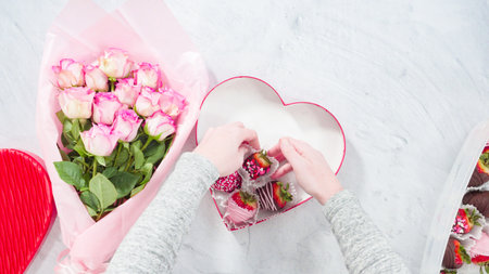 Flat lay. Step by step. Bouquet of pink roses with a box of chocolate dipped strawberries.の写真素材