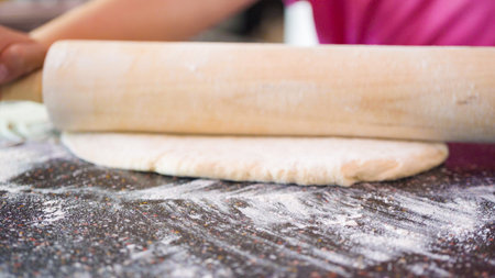 Little girl rolling out pizza dough for individual small pizzas.