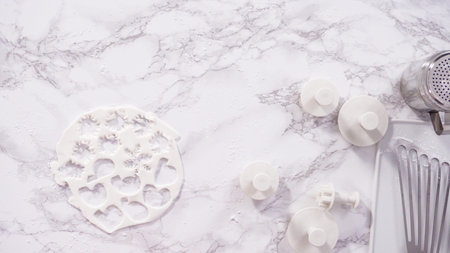 Flat lay. Step by step. Cutting out snowflakes with cookie cutters out of white fondant on a marble...