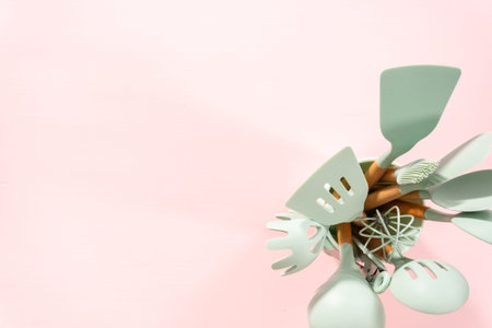 Flat lay. New blue silicone kitchen utensils with wooden handles on a pink background.