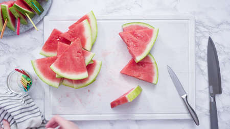 Flat lay. Slicing red watermelon into small pieces on a white cutting board.の写真素材