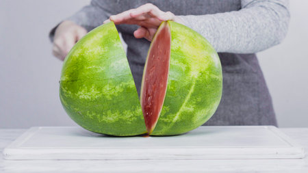 Slicing red watermelon into small pieces on a white cutting board.
