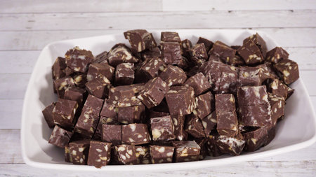 Step by step. Macadamia fudge cut in small cubes on a white serving dish.