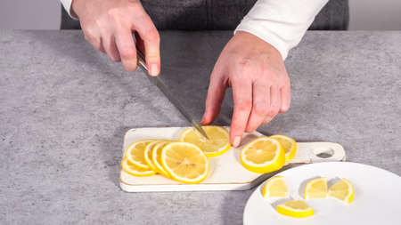 Step by step. Slicing organic lemon wedges on a white plate.の写真素材