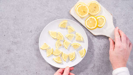 Flat lay. Step by step. Slicing organic lemon wedges on a white plate.の写真素材