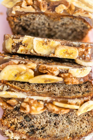 Sliced loaf of banana nut bread drizzled homemade caramel on a pink cutting board.の写真素材