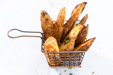Freshly baked potato wedges with spices in a wire basket.