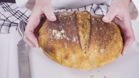 Slicing freshly baked sourdough wheat bread on a white cutting board.