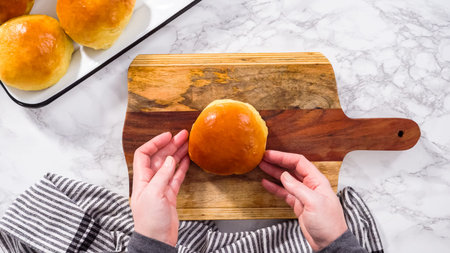 Flat lay. Step by step. Slicing freshly baked brioche bun on a wood cutting board.の写真素材
