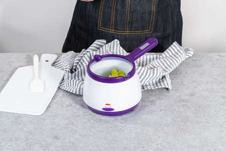 Melting color chocolate chips in a candy melting pot to make carrot chocolate-covered pretzels.の写真素材