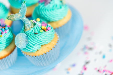 Gourmet mermaid cupcakes topped with blue buttercream frosting and decorated with sprinkles and chocolate mermaid tails.の写真素材