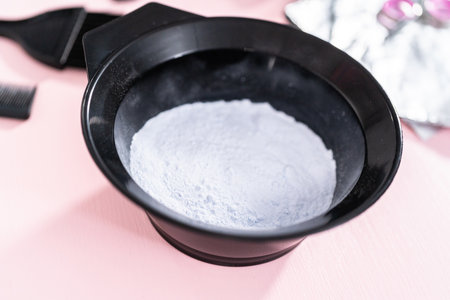 Hair color dye powder in a black plastic mixing bowl on a pink background.の写真素材