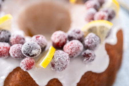 Lemon cranberry bundt cake decorated with sugar cranberries and lemon wedges on a cake stand.の写真素材