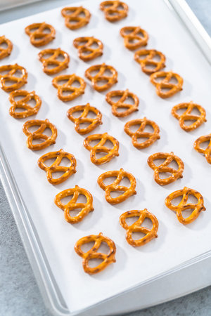 Mini pretzel twists lined on a baking sheet with parchment paper to prepare Easter chocolate-covered pretzel bunnies and ducklings.の写真素材