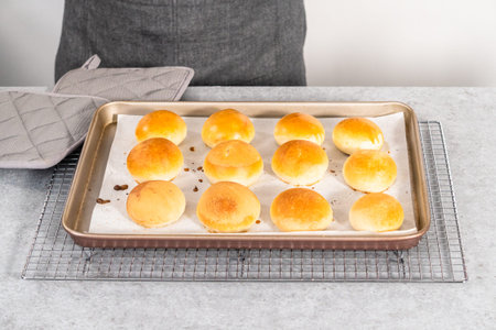 Freshly baked dinner rolls with an egg wash on a baking sheet lined with parchment paper.の写真素材