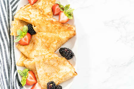 Flat lay. Freshly baked crepes folded in triangles and garnished with berries on a serving plate.の写真素材